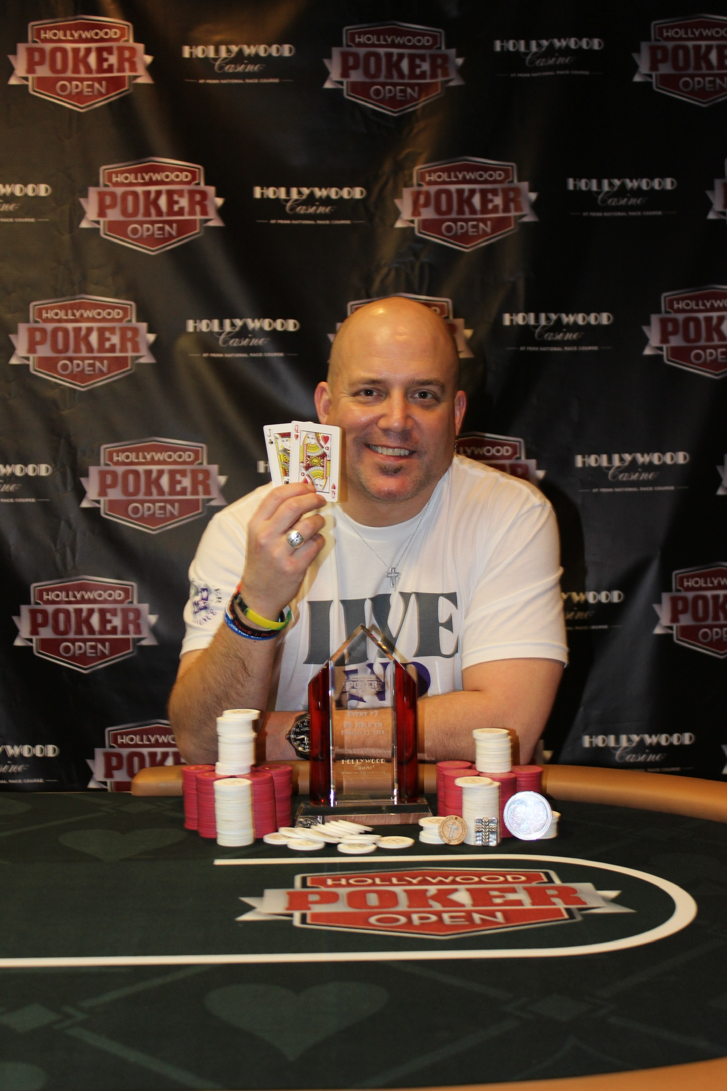 Lee Childs holding jack queen beside a Hollywood Poker Open trophy